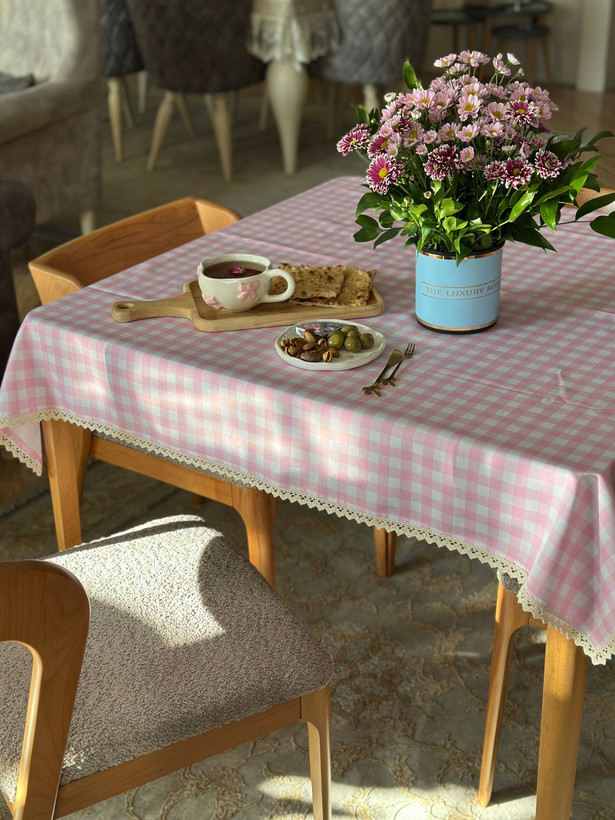 رومیزی چهارخانه صورتی روشن نواردوزی شده روی میز ناهارخوری با گلهای صورتی